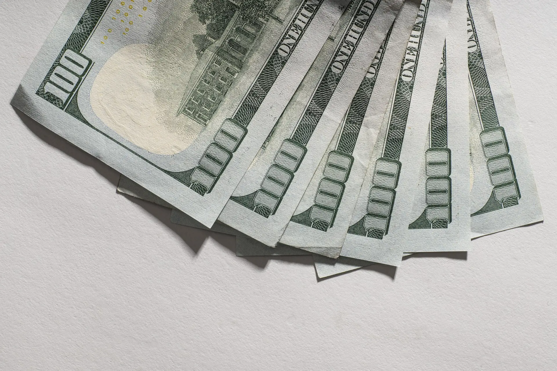 Billetes de cien dólares abiertos en abanico sobre una mesa blanca