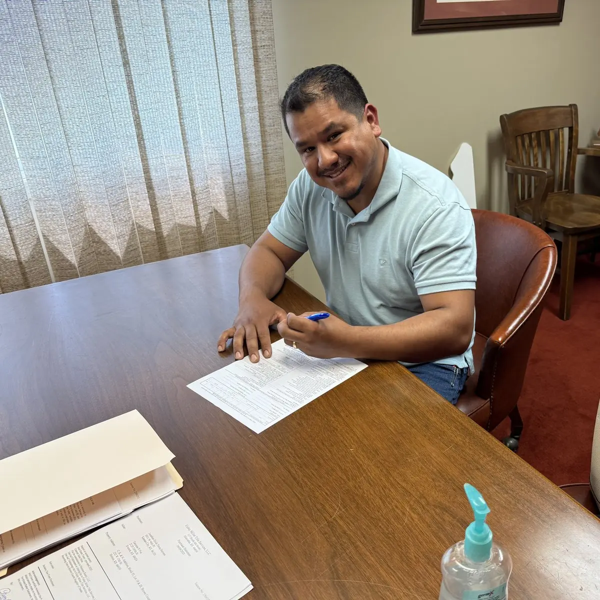 Un hombre sonríe mientras firma un documento en la mesa de una oficina