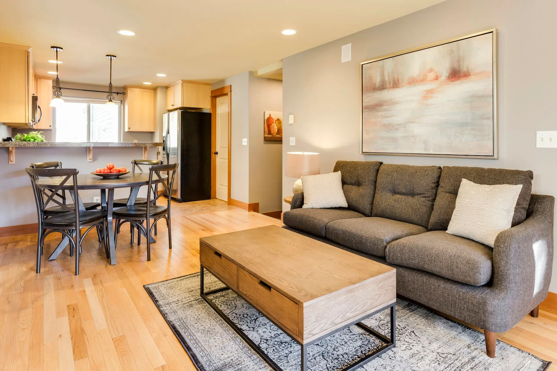 Una sala ordenada con sillón gris, mesa de centro y el comedor detrás
