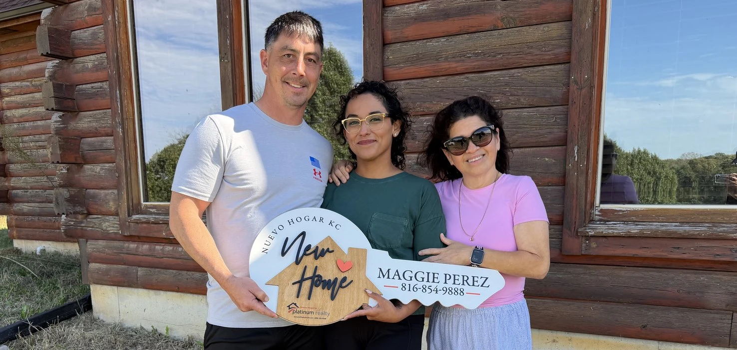 Pareja cliente y Maggie Perez con el letrero de llave de Nuevo Hogar KC frente a su cabaña